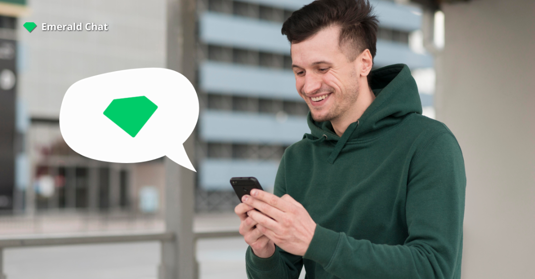 Smiling man in a green hoodie using his phone with a chat bubble featuring the Emerald Chat logo, representing modern online chat room alternatives.